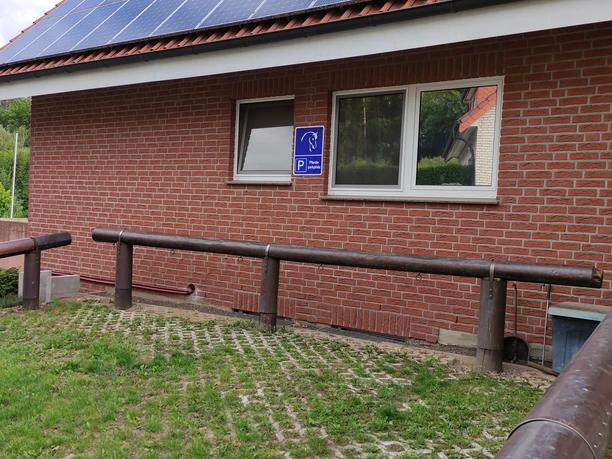 Behinderten-Parkplatz bei einem roten Backsteingebäude mit einem Holzgeländer im Vordergrund.