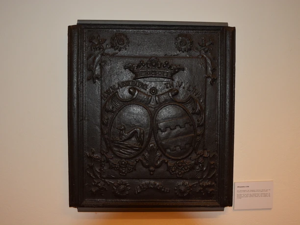 Wappenrelief aus schwarzem Metall mit filigranen Details, zwei Wappenmotiven und floralen Verzierungen.