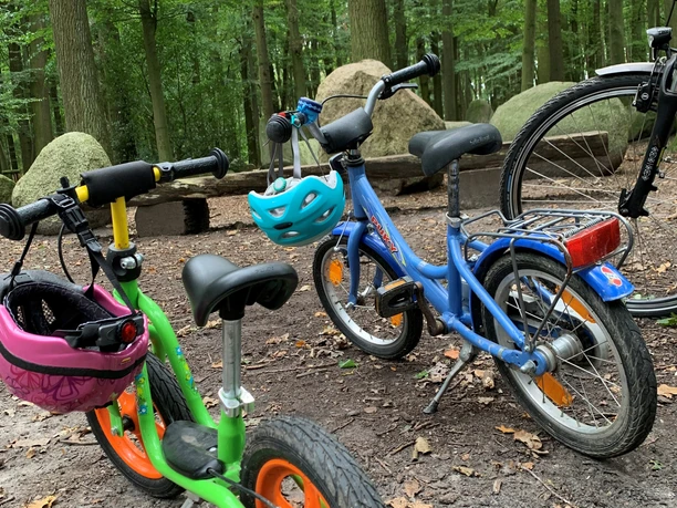 Kinderräder stehen im Grünen des Findlingswaldes Neuenknick, umgeben von Bäumen und Felsen.