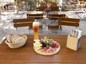 Liebevoll angerichteter Brotzeitteller mit Schinken, Wurst, Käse und Salatgarnitur, dazu ein gefüllter Brotkorb und ein frisch gezapftes Bier