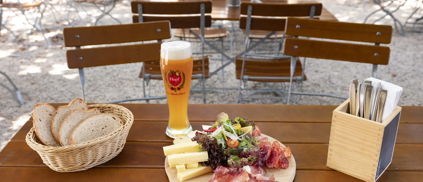 Liebevoll angerichteter Brotzeitteller mit Schinken, Wurst, Käse und Salatgarnitur, dazu ein gefüllter Brotkorb und ein frisch gezapftes Bier