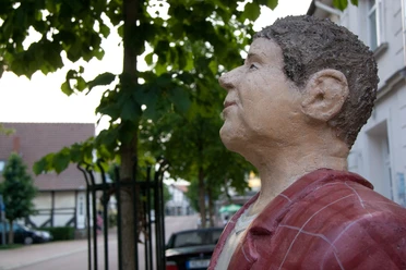 Lechnerfigur "Herr Meier" Lechnerfigur "Herr Meier" unter einem Baum, mit Fachwerkhäusern im Hintergrund.