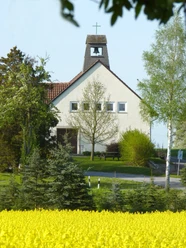 Kirche Bierde Eine kleine, weiß verputzte Kirche mit Glockenturm vor blühendem Rapsfeld, flankiert von Bäumen.