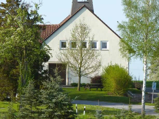 Kirche Bierde Eine kleine, weiß verputzte Kirche mit Glockenturm vor blühendem Rapsfeld, flankiert von Bäumen.