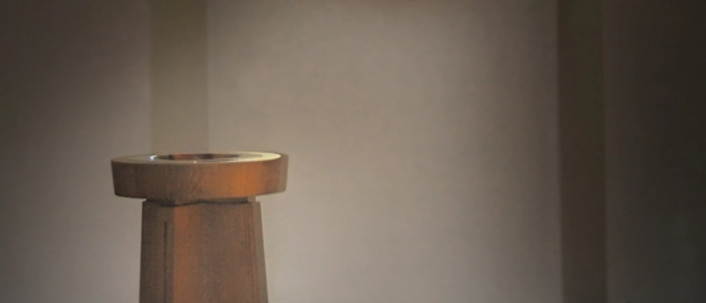 Ein Taufstein vor einem Rundfenster, dessen buntes Glas ein farbenfrohes Muster auf den Boden projiziert.