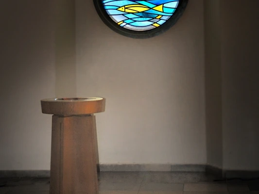 Kirche Bierde Taufstein Ein Taufstein vor einem Rundfenster, dessen buntes Glas ein farbenfrohes Muster auf den Boden projiziert.