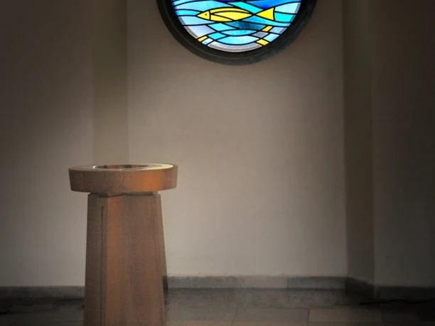 Kirche Bierde Taufstein Ein Taufstein vor einem Rundfenster, dessen buntes Glas ein farbenfrohes Muster auf den Boden projiziert.