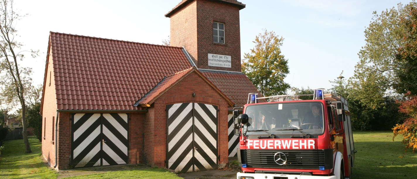 Ein rotes Feuerwehrfahrzeug vor einem Backsteingebäude mit typischen schwarz-weißen Toren.