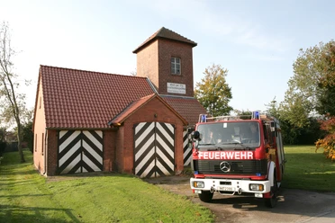 Feuerwehrgerätehaus Bierde Ein rotes Feuerwehrfahrzeug vor einem Backsteingebäude mit typischen schwarz-weißen Toren.