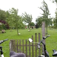 Erlebniswald Bierde Zwei Fahrräder stehen vor einem Holztor, dahinter eine grüne Wiese mit jungen Bäumen und Spaziergängern.