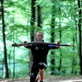 Fitness-Wanderung mit Trainer Robert Dreisiebner Trainer Robert Dreisiebner führt eine Übung im Wald aus, umgeben von hohen Bäumen und grünem Laub.