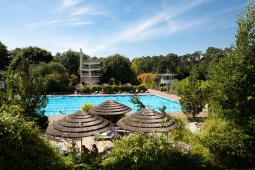 Waldbad in Hilden Freibad mit Schwimmbecken, Rutschen und Strohdächern, umgeben von dichten Bäumen im Waldbad Hilden.