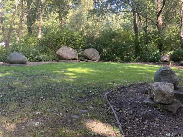 Große Findlinge liegen auf einer von Bäumen gesäumten Wiese und bieten einen harmonischen Anblick.