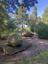 Große Findlinge auf Sandwegen in einem grünen Park, umgeben von Bäumen und Sträuchern.