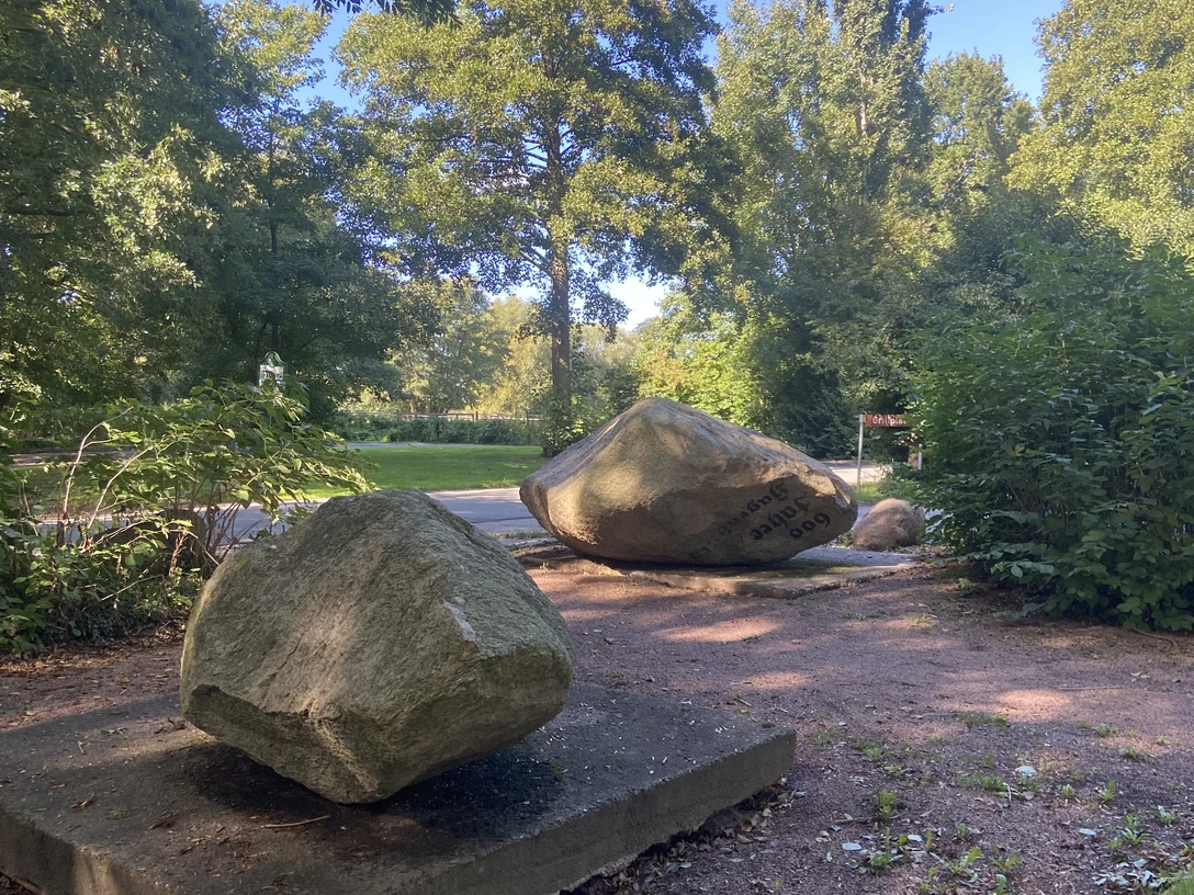 Findlingsgarten Große Findlinge auf Sandwegen in einem grünen Park, umgeben von Bäumen und Sträuchern.