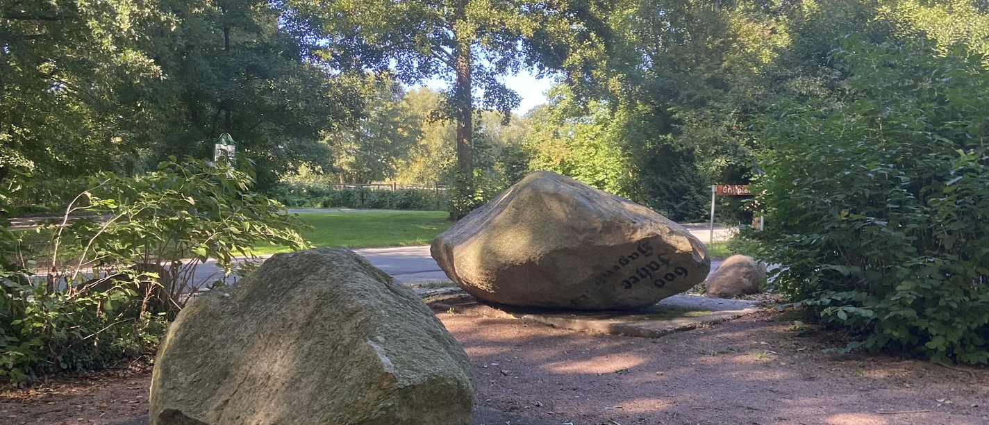 Findlingsgarten Große Findlinge auf Sandwegen in einem grünen Park, umgeben von Bäumen und Sträuchern.