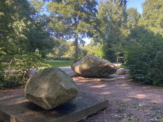 Findlingsgarten Große Findlinge auf Sandwegen in einem grünen Park, umgeben von Bäumen und Sträuchern.