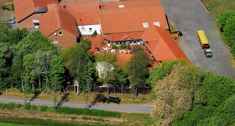 Wiehes Planwagenfahrten Luftaufnahme eines Bauernhofs mit roten Dächern, umgeben von Bäumen; ein Planwagen steht bereit.