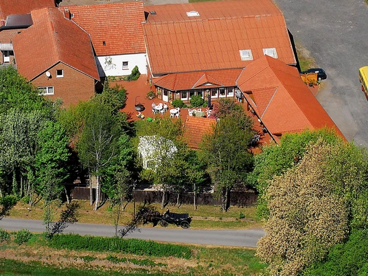 Wiehes Planwagenfahrten Luftaufnahme eines Bauernhofs mit roten Dächern, umgeben von Bäumen; ein Planwagen steht bereit.