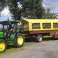 Wiehes_Planwagen_1_c33e30a3c9.jpg Grüner Traktor zieht einen gelben Planwagen über einen gepflasterten Weg, Bäume im Hintergrund.