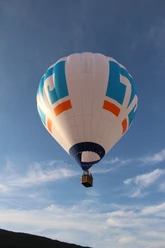 Heißluftballon_Ballonteam am Wiehen Heißluftballon schwebt friedlich über einer hügeligen Landschaft, vor einem blauen Himmel mit Wolken.