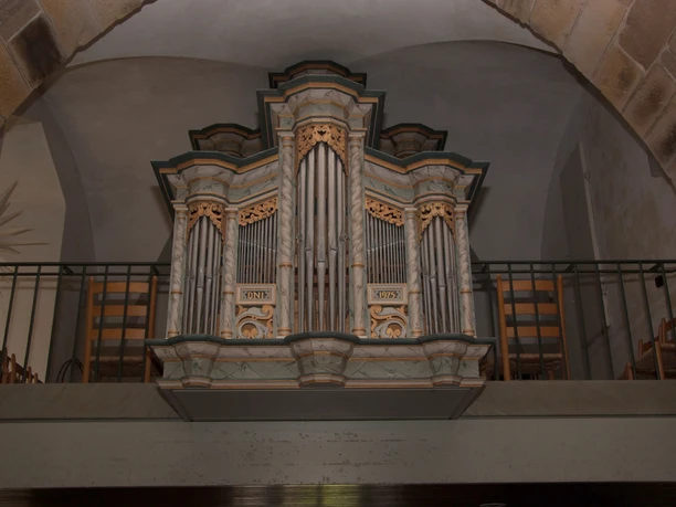 Historische Orgelempore mit kunstvoll geschnitzten Holzdetails in einer Kirche mit gewölbten Decken.