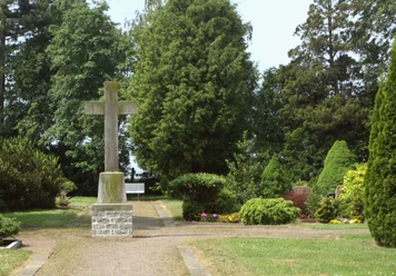 Friedhof Buchholz Ein großzügiger Friedhof mit einem steinernen Kreuz, umgeben von grünen Bäumen und gepflegten Pflanzen.