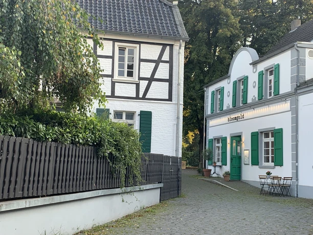 Restaurant bloomgold in Monheim am Rhein Restaurant bloomgold in Monheim am Rhein mit weißer Fassade, grünen Fensterläden und Kopfsteinpflaster.