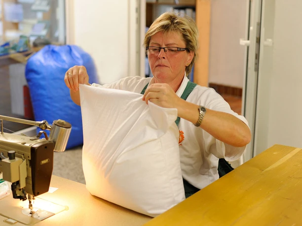 Žena sedí u šicího stroje ve výrobně postelí na husí farmě Eskildsen a plní polštář peřím, regionálními produkty.