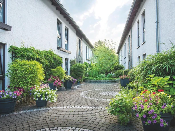 Hotel am Wald in Mohnheim am Rhein Gepflegter, mit Pflanzen gesäumter Innenhof zwischen zwei weißen Gebäuden, entspannende Atmosphäre.