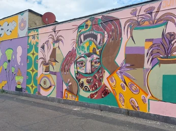 Arty Farty Gallery Ein leuchtendes Wandgemälde aus bunten Formen und Figuren schmückt die Mauer einer urbanen Straße.A bright mural of colorful shapes and figures adorns the wall of an urban street.