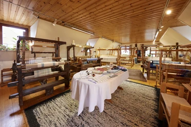 In einem lichtdurchfluteten Raum stehen mehrere historische Webstühle auf einem Holzfußboden.