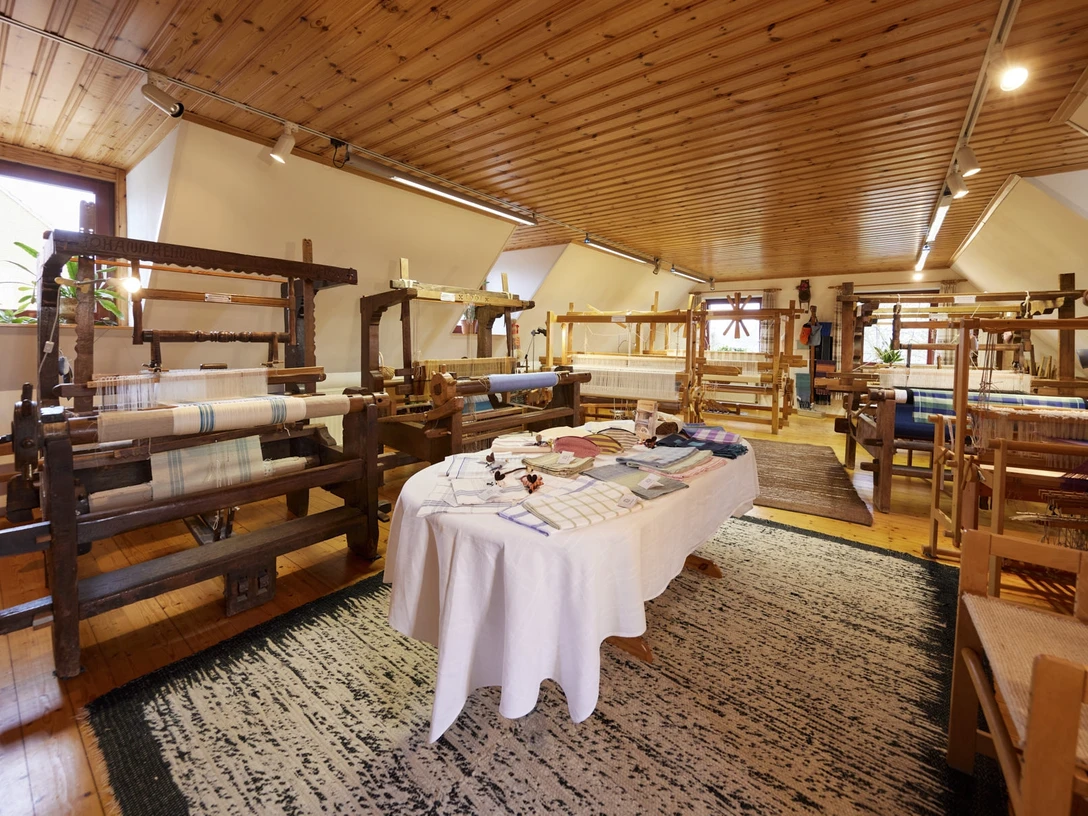 In einem lichtdurchfluteten Raum stehen mehrere historische Webstühle auf einem Holzfußboden.