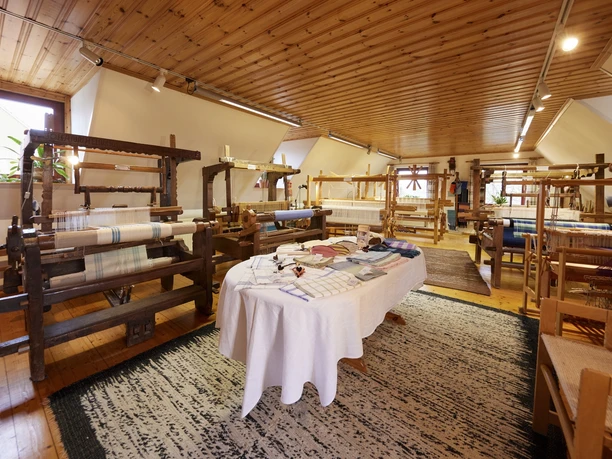 In einem lichtdurchfluteten Raum stehen mehrere historische Webstühle auf einem Holzfußboden.