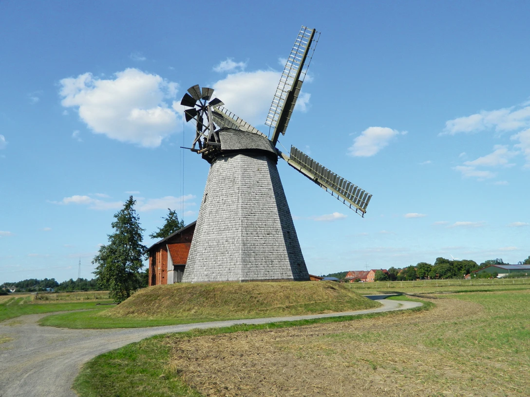 Windmühle Bierde Windmühle Bierde mit grauem Holzschindeldach und Flügeln in einer weiten, grünen Landschaft.