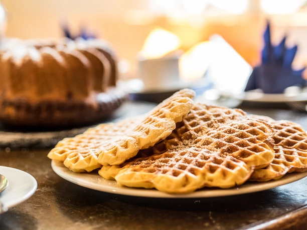 Bergische Kaffeetafel Waffeln mit Puderzucker auf einem Teller; im Hintergrund Kuchen und Kaffeetassen.