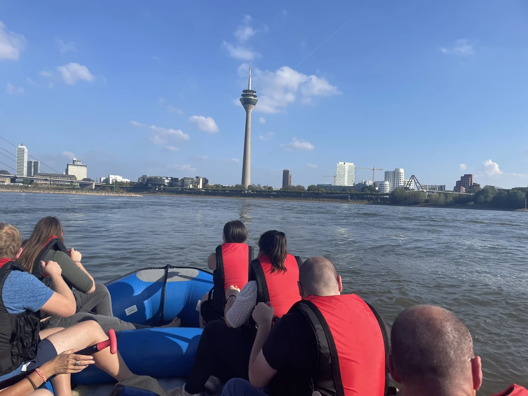 Meyer-Rafting Menschen auf einem Schlauchboot mit roten Schwimmwesten fahren auf einem Fluss Richtung Fernsehturm.
