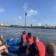 Meyer-Rafting Menschen auf einem Schlauchboot mit roten Schwimmwesten fahren auf einem Fluss Richtung Fernsehturm.