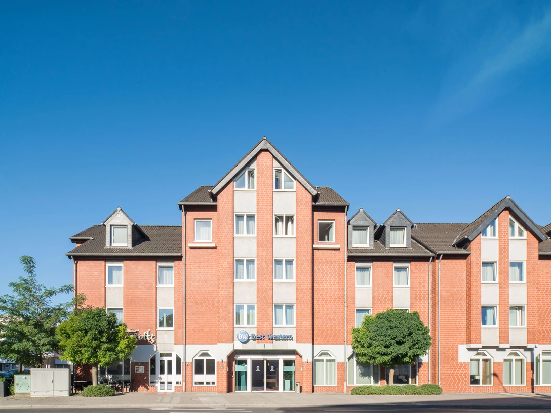 Best Western Hotel Breitbach in Ratingen Rotes Backsteinhotel mit spitzem Giebel, umrahmt von Bäumen, unter klarem, blauem Himmel.