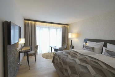 Essensio Hotel in Erkrath Ein modernes Hotelzimmer mit Doppelbett, Schreibtisch, Fernseher, Vorhängen und gemütlichen Sitzgelegenheiten.