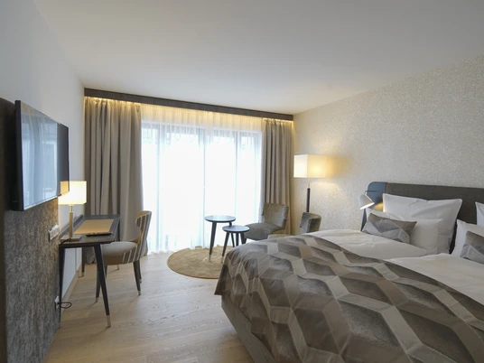 Essensio Hotel in Erkrath Ein modernes Hotelzimmer mit Doppelbett, Schreibtisch, Fernseher, Vorhängen und gemütlichen Sitzgelegenheiten.
