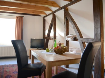 Gästezimmer Hof Karpenhaus in Ratingen Ein Gästezimmer mit Holzbalken, Esstisch, zwei Stühlen, einem Fernseher und zwei Einzelbetten.