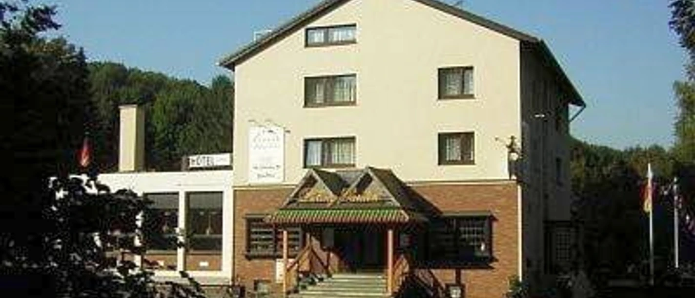 Hotel Talburg in Heiligenhaus Vierstöckiges, rechteckiges Hotelgebäude mit hellem Anstrich, umgeben von Bäumen, Eingang mit Vordach.