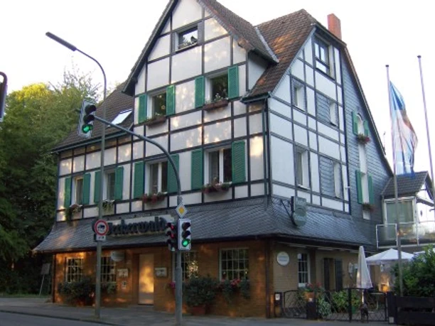 Gästewohnung Werkerwald in Heiligenhaus Fachwerkhaus mit grünen Fensterläden und großem Dach in Heiligenhaus. Verkehrsampeln im Vordergrund.