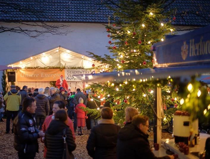 Menschen versammeln sich bei weihnachtlichem Marktstand am Abend, dekoriert mit Lichtern und Tannenbaum.