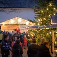 Adventsplaetzchen.jpg Menschen versammeln sich bei weihnachtlichem Marktstand am Abend, dekoriert mit Lichtern und Tannenbaum.