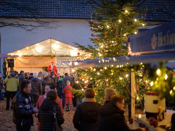 Menschen versammeln sich bei weihnachtlichem Marktstand am Abend, dekoriert mit Lichtern und Tannenbaum.