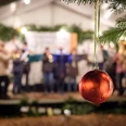 Rote Weihnachtskugel im Vordergrund, im Hintergrund unscharfe Live-Musikgruppe bei abendlicher Festbeleuchtung.