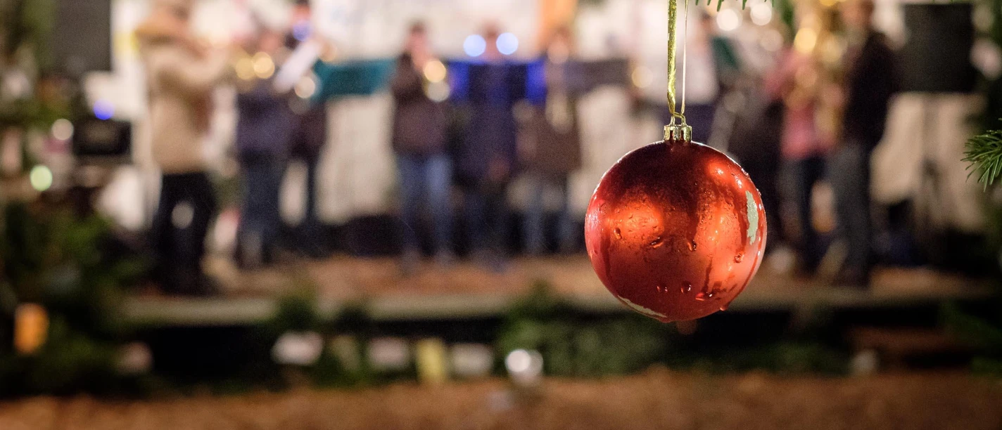 Rote Weihnachtskugel im Vordergrund, im Hintergrund unscharfe Live-Musikgruppe bei abendlicher Festbeleuchtung.