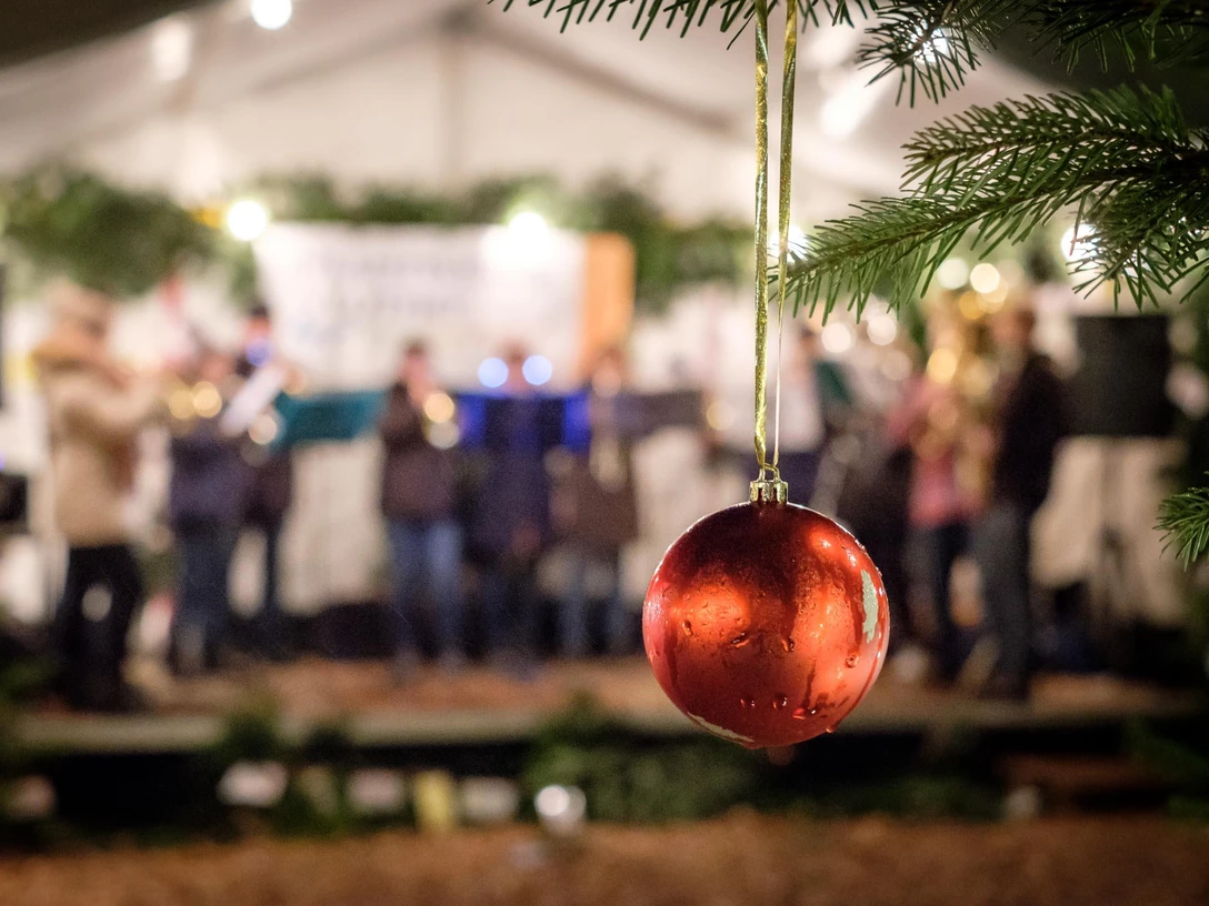 Adventsplaetzchen.jpg Rote Weihnachtskugel im Vordergrund, im Hintergrund unscharfe Live-Musikgruppe bei abendlicher Festbeleuchtung.